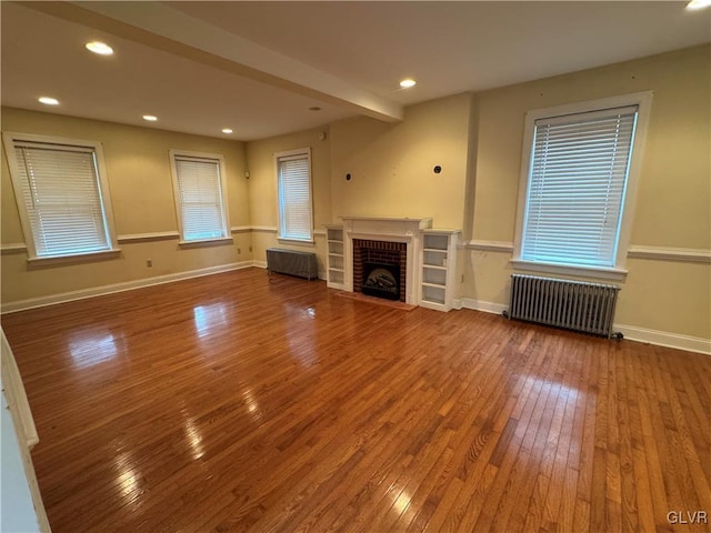 unfurnished living room featuring baseboards, wood-type flooring, radiator, and radiator heating unit