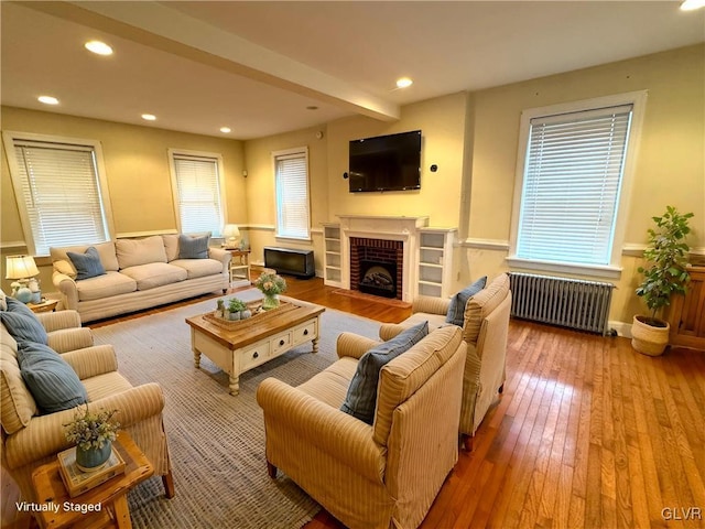 living area with radiator heating unit, a fireplace, recessed lighting, and wood-type flooring