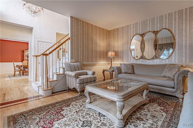 living area with a wainscoted wall, stairway, wood finished floors, a chandelier, and wallpapered walls