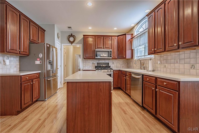 kitchen featuring light countertops, appliances with stainless steel finishes, a kitchen island, a sink, and light wood-type flooring