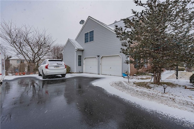 view of snowy exterior featuring driveway and an attached garage