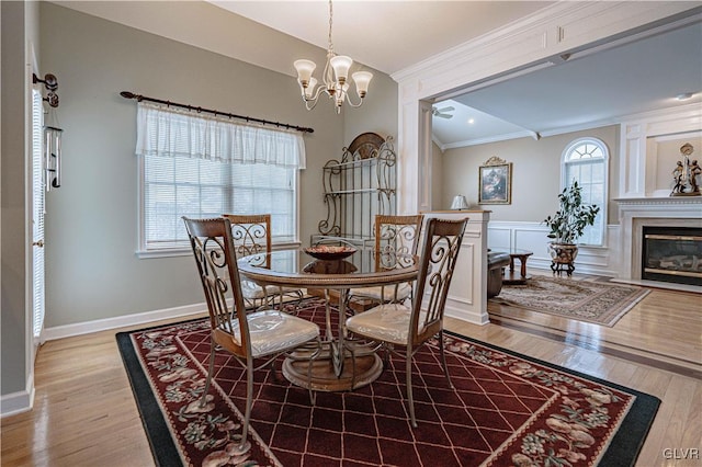 dining space with ornamental molding, a glass covered fireplace, light wood-style flooring, and a decorative wall