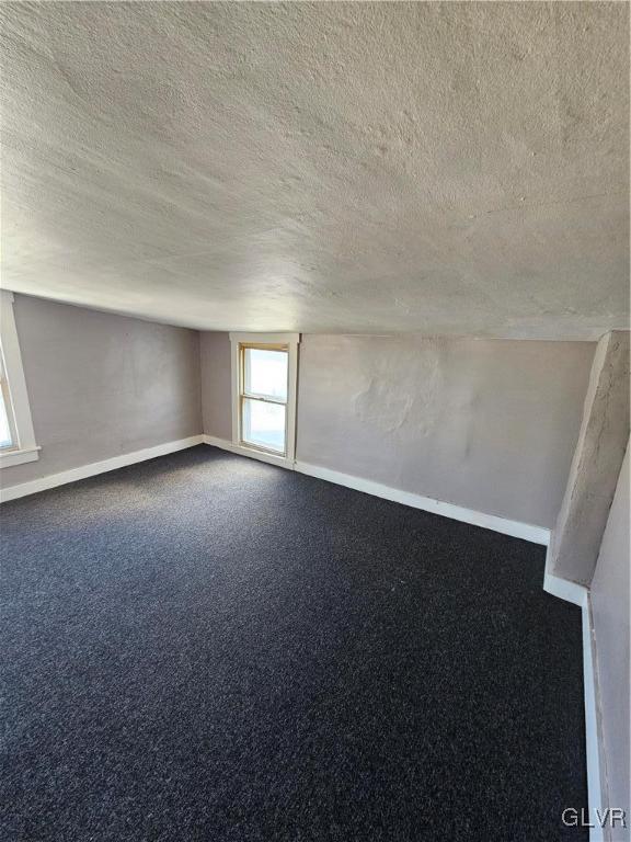 unfurnished room with a textured ceiling, carpet floors, and baseboards