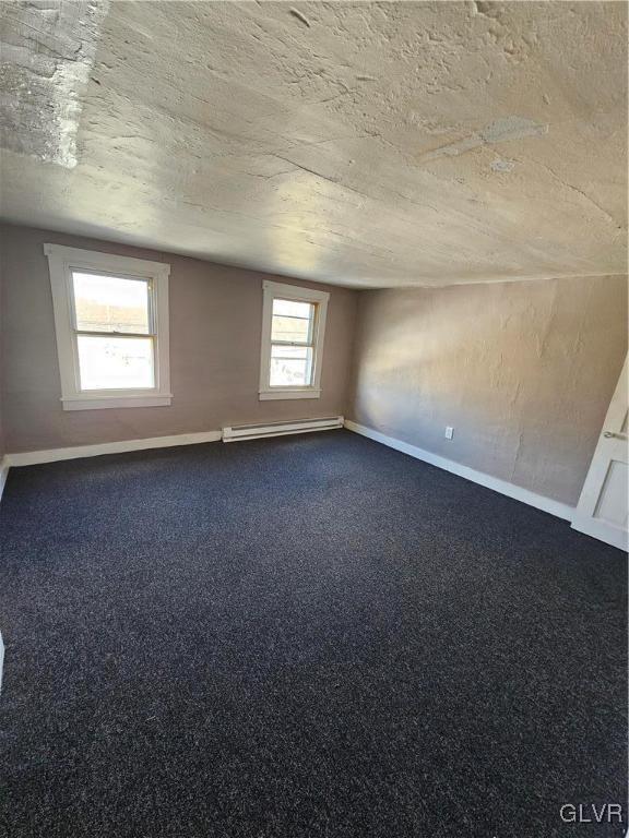 carpeted spare room featuring a baseboard heating unit, a textured ceiling, and baseboards