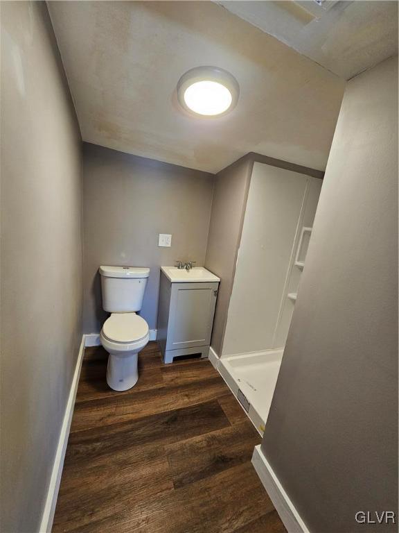 bathroom with baseboards, a shower stall, toilet, and wood finished floors