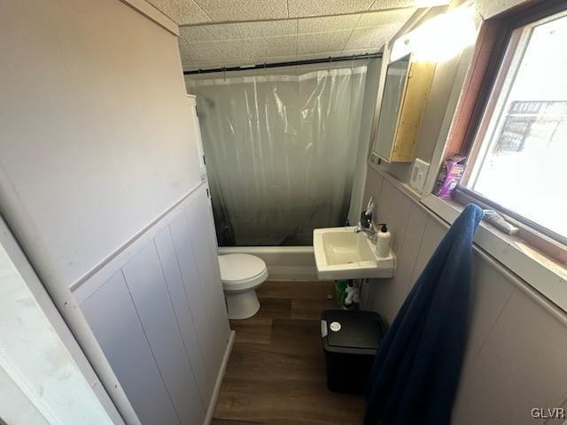 bathroom with toilet, a wainscoted wall, wood finished floors, a sink, and shower / bath combination with curtain