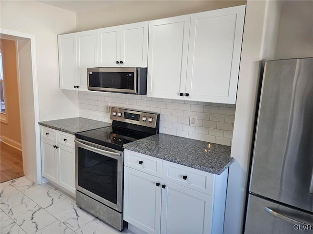 kitchen with decorative backsplash, appliances with stainless steel finishes, dark stone countertops, marble finish floor, and white cabinetry