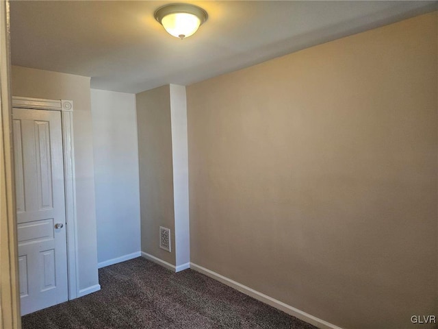 spare room with dark carpet, visible vents, and baseboards