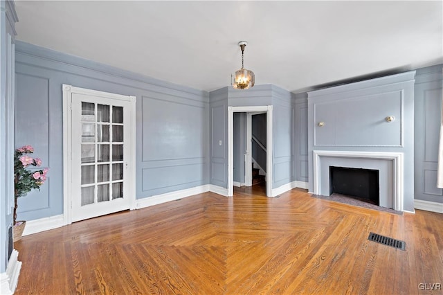 unfurnished living room with a fireplace with flush hearth, visible vents, a decorative wall, and stairway