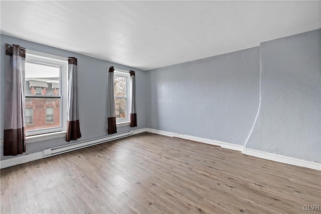 unfurnished room featuring baseboards, baseboard heating, and wood finished floors