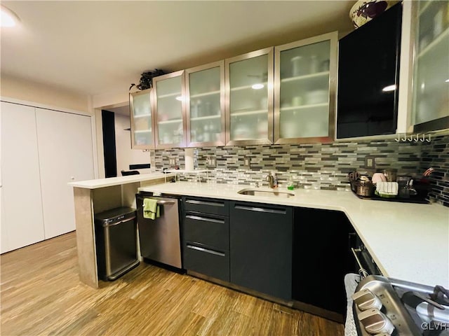 kitchen with decorative backsplash, glass insert cabinets, a sink, light countertops, and stainless steel dishwasher