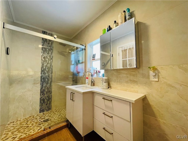 bathroom featuring wood finished floors, vanity, tile walls, ornamental molding, and a stall shower