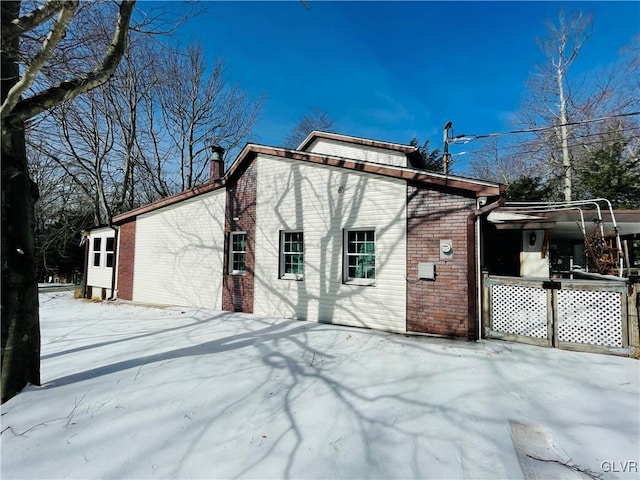 snow covered property featuring brick siding and a chimney