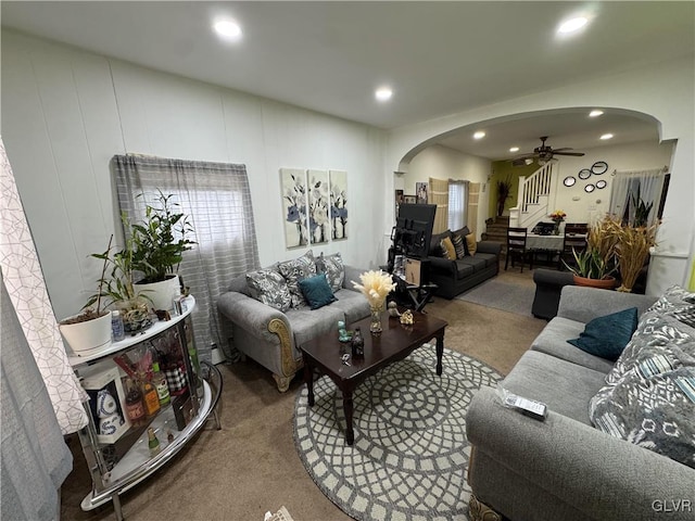 living area featuring arched walkways, carpet flooring, ceiling fan, and stairs