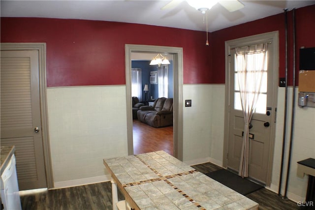 interior space with a wainscoted wall, a ceiling fan, tile walls, and dark wood-style flooring