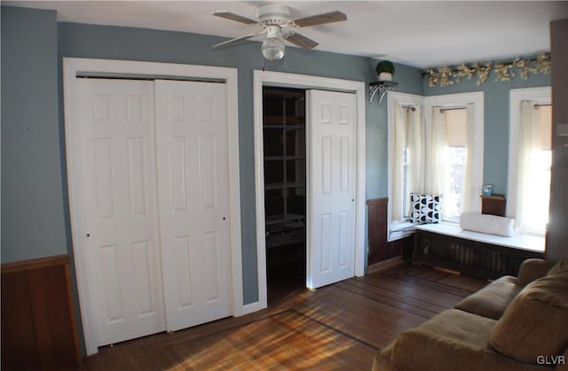 living area featuring dark wood-style floors, a ceiling fan, and a wainscoted wall