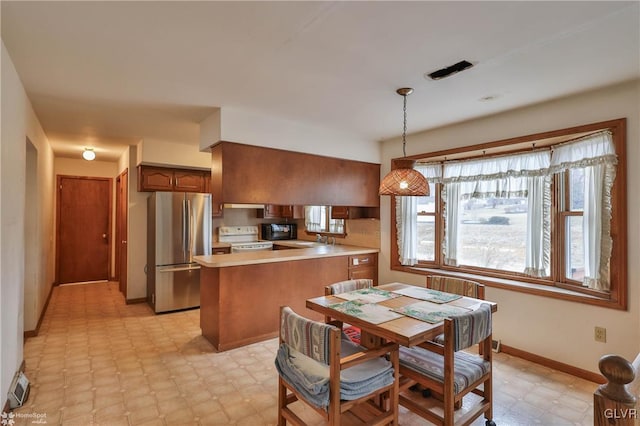 kitchen with pendant lighting, white range with electric cooktop, light countertops, freestanding refrigerator, and a peninsula