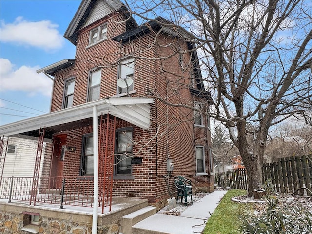 snow covered property with a porch, brick siding, and fence