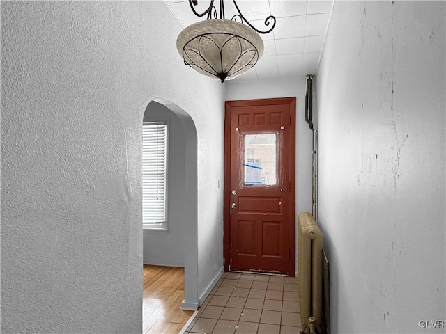 doorway with arched walkways, a textured wall, a healthy amount of sunlight, and radiator