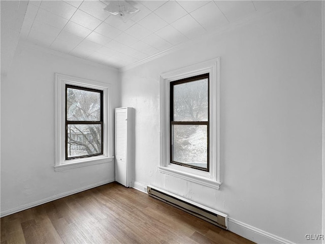 spare room featuring a baseboard radiator, baseboards, wood finished floors, and ornamental molding