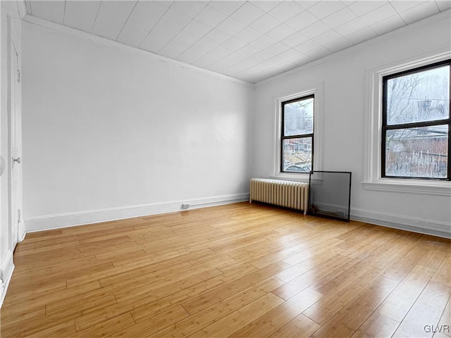 spare room featuring radiator, light wood-type flooring, ornamental molding, and baseboards