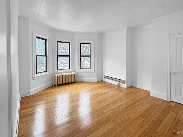 empty room featuring a baseboard radiator, baseboards, light wood finished floors, and radiator heating unit