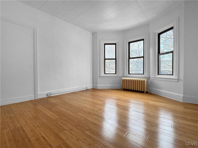 unfurnished room with light wood-style floors, baseboards, and radiator heating unit