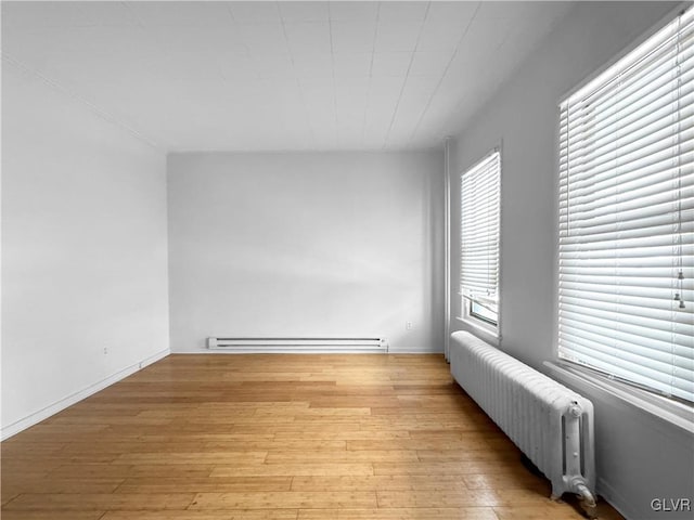 empty room featuring radiator, light wood finished floors, and a baseboard radiator