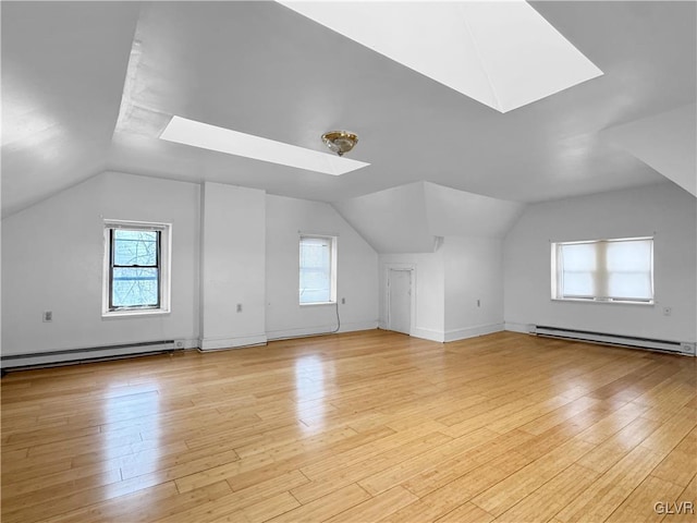 additional living space featuring light wood-type flooring, vaulted ceiling with skylight, and a baseboard radiator