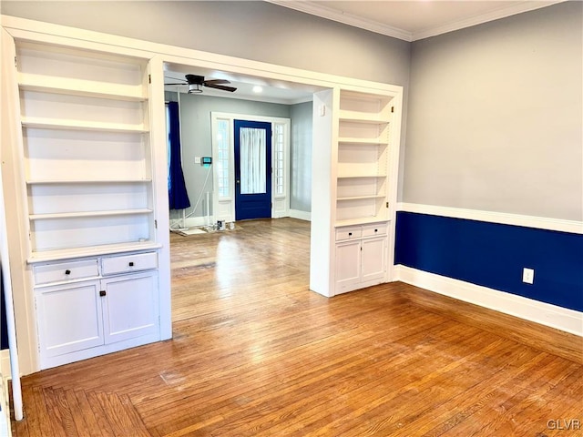 spare room with baseboards, built in features, a ceiling fan, ornamental molding, and light wood-style floors