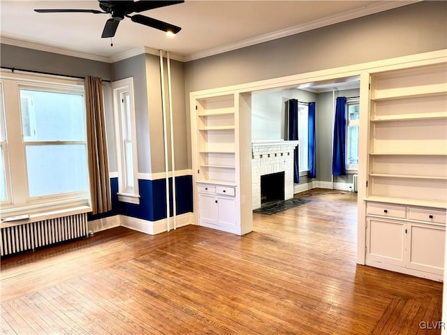 unfurnished living room with baseboards, radiator heating unit, crown molding, light wood-type flooring, and a fireplace