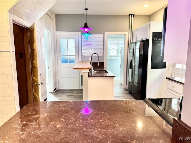 kitchen with white cabinetry, a sink, hanging light fixtures, and black refrigerator with ice dispenser