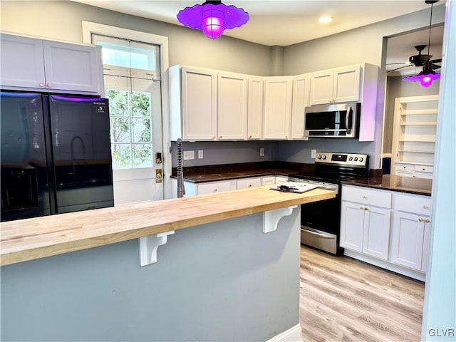 kitchen featuring butcher block countertops, white cabinetry, appliances with stainless steel finishes, a kitchen bar, and decorative light fixtures