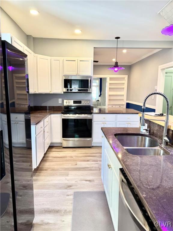 kitchen with white cabinets, appliances with stainless steel finishes, dark stone countertops, hanging light fixtures, and a sink