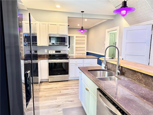 kitchen with decorative light fixtures, stainless steel appliances, light wood-style floors, white cabinetry, and a sink