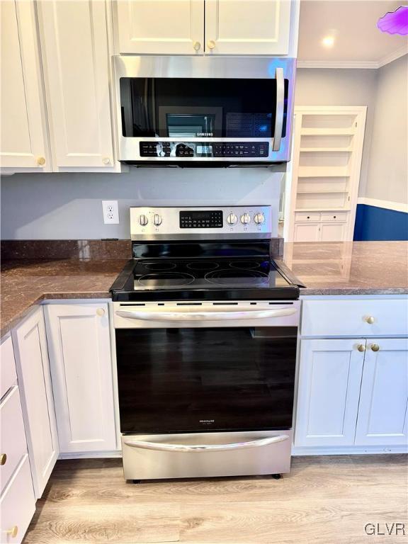 kitchen featuring white cabinets, ornamental molding, stainless steel appliances, and dark stone countertops