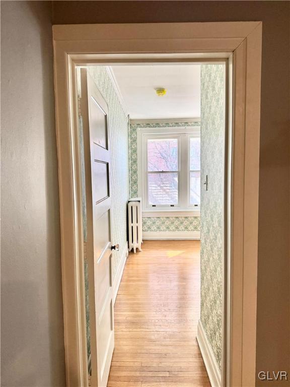 corridor with baseboards, radiator heating unit, light wood-type flooring, and wallpapered walls