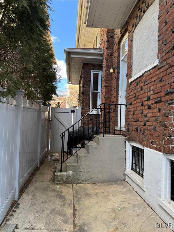 doorway to property with a gate, brick siding, and fence