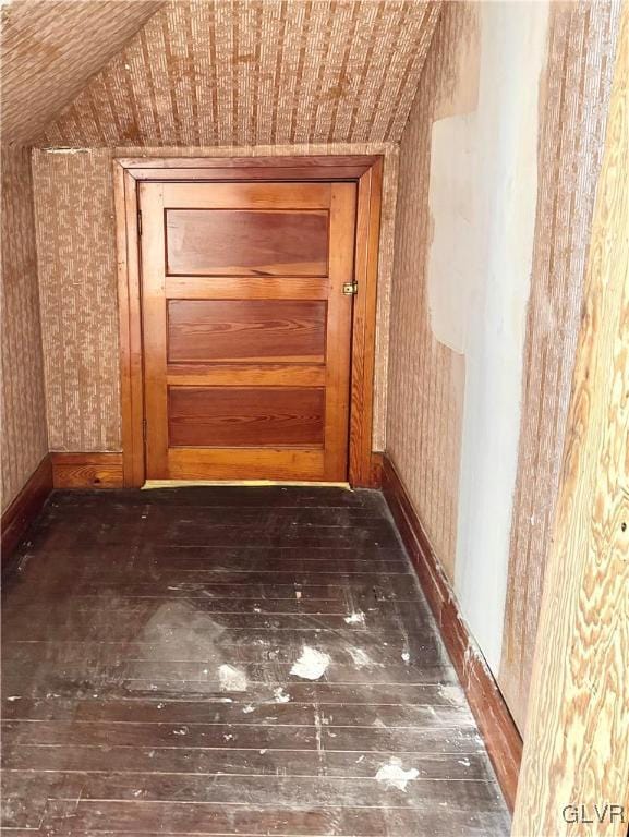 hallway featuring wallpapered walls, vaulted ceiling, baseboards, and dark wood finished floors