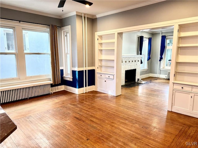 unfurnished bedroom featuring light wood finished floors, radiator heating unit, ornamental molding, a brick fireplace, and baseboards