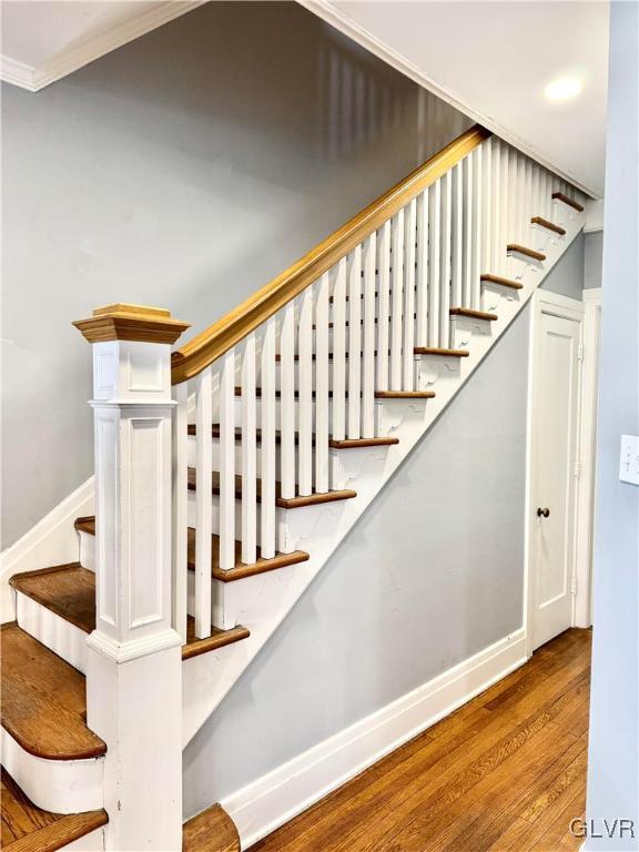 staircase with crown molding, baseboards, and wood finished floors