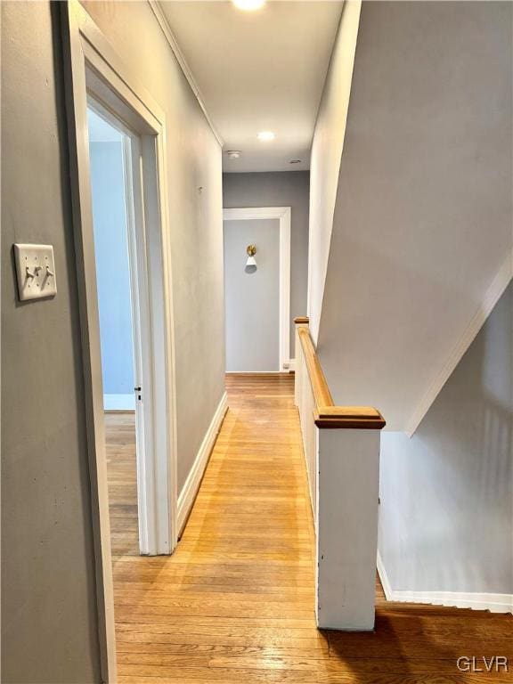 hall featuring light wood-type flooring, an upstairs landing, and baseboards