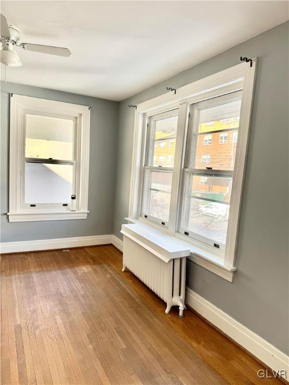 spare room featuring baseboards, ceiling fan, radiator heating unit, and light wood-style floors