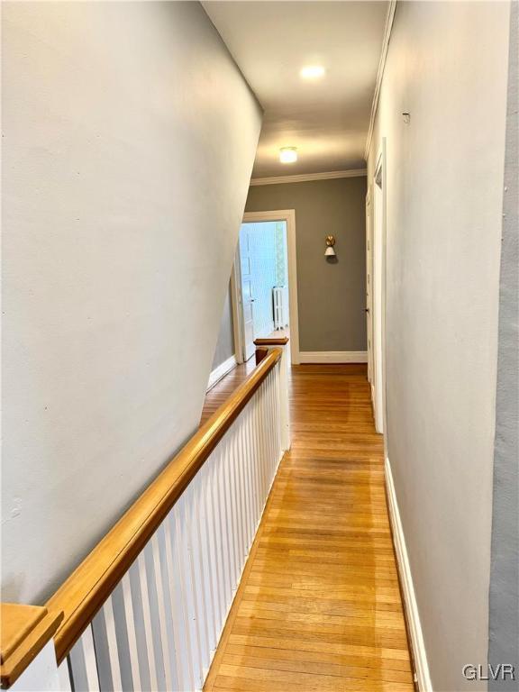 hallway with light wood finished floors, baseboards, and ornamental molding