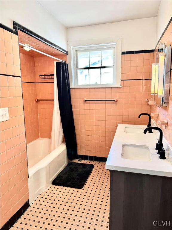 full bath featuring a sink, double vanity, shower / bath combo with shower curtain, and tile walls