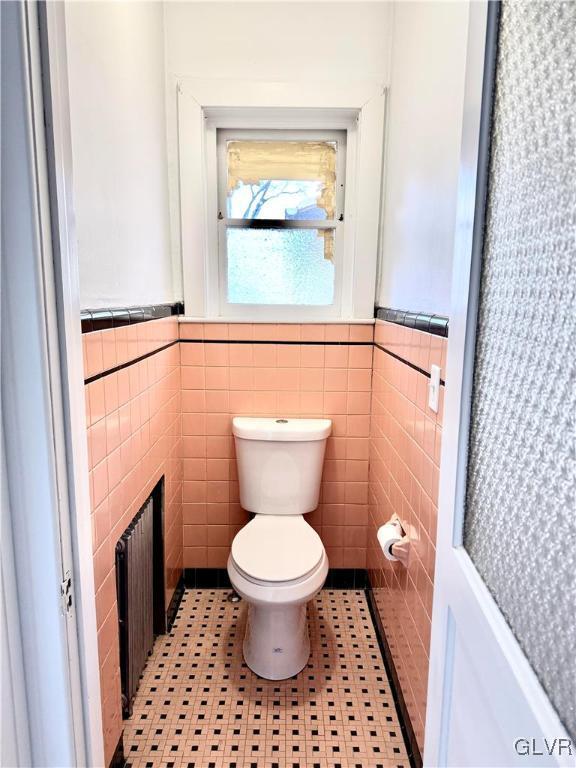 bathroom with radiator heating unit, wainscoting, toilet, and tile walls