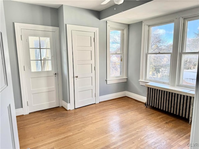 interior space featuring baseboards, light wood-style floors, a ceiling fan, and radiator