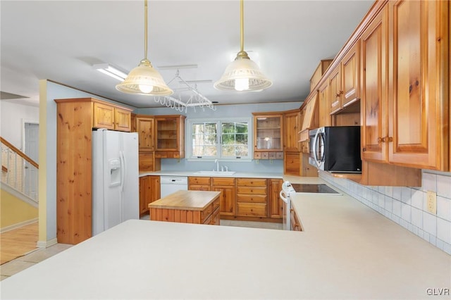 kitchen featuring pendant lighting, light countertops, a sink, white appliances, and a peninsula