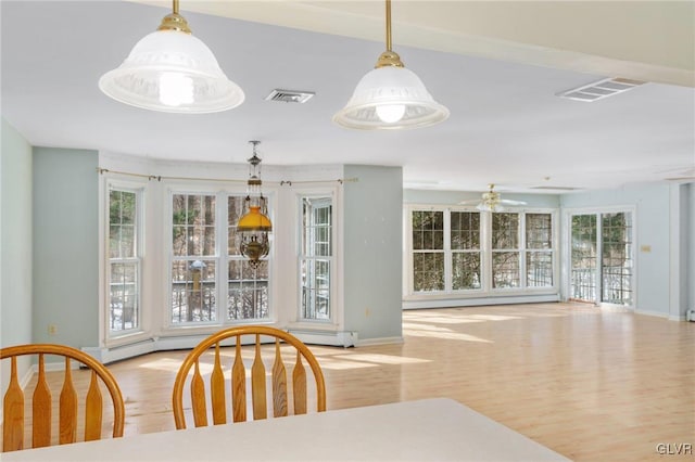 dining space featuring light wood finished floors, a baseboard radiator, visible vents, and baseboards