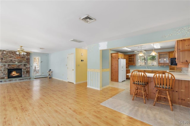 kitchen featuring open floor plan, brown cabinetry, white fridge with ice dispenser, stainless steel microwave, and glass insert cabinets